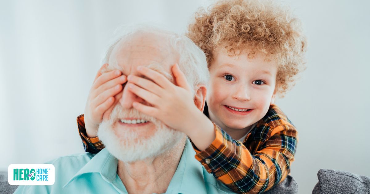Grandchild playfully covering grandfather&rsquo;s eyes, showing the joy of in-person socializing for seniors.