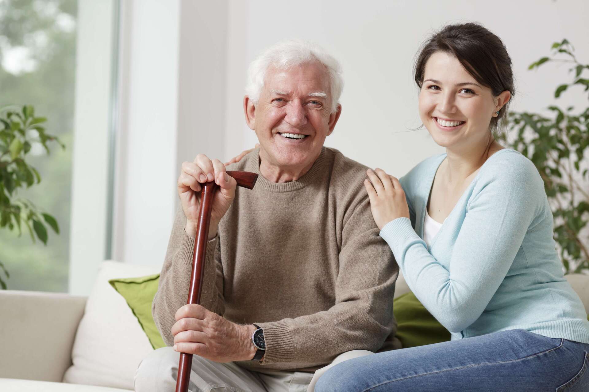 Caregiver hugging an elderly man holding a cane.