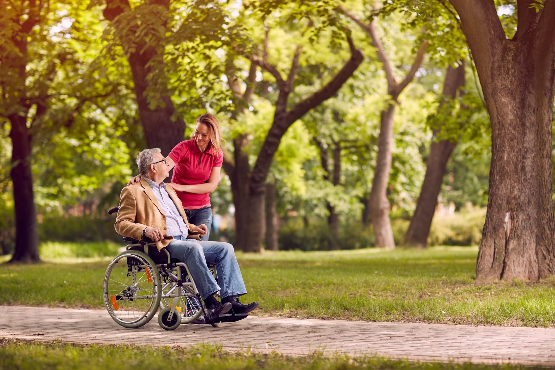 Image of a lady looking at an elderly person sitting in a wheelchair in the park.