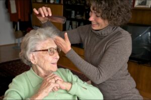 Image of home caregiver hair combing an elderly lady at home.