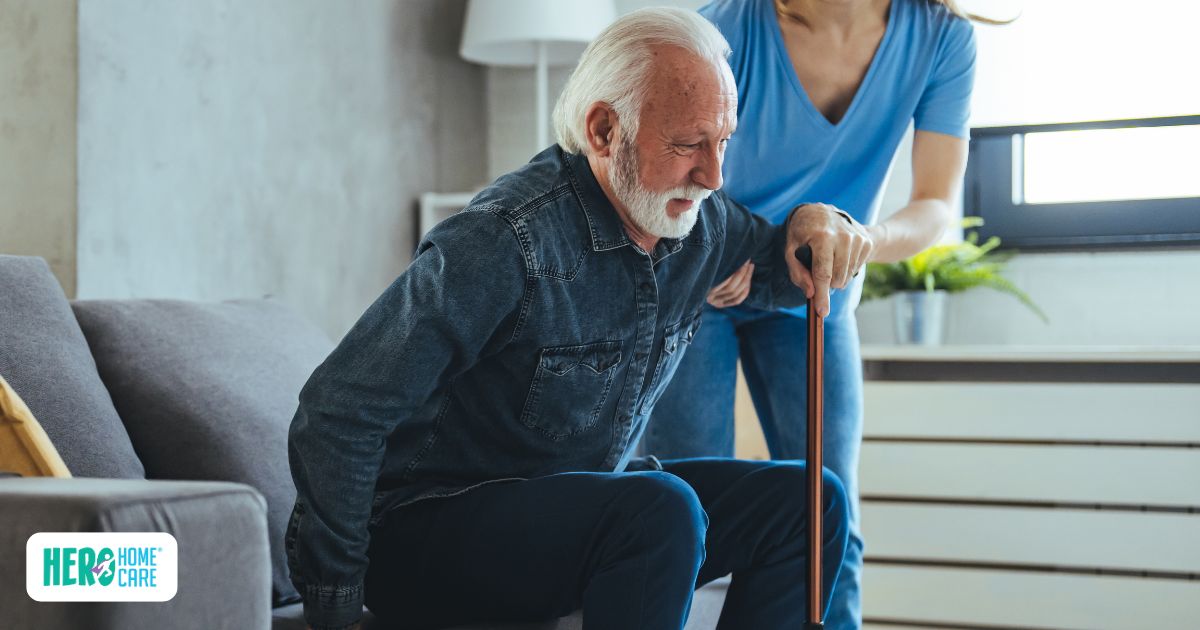 An elderly man being supported by a caregiver while standing, showing mobility challenges at home.