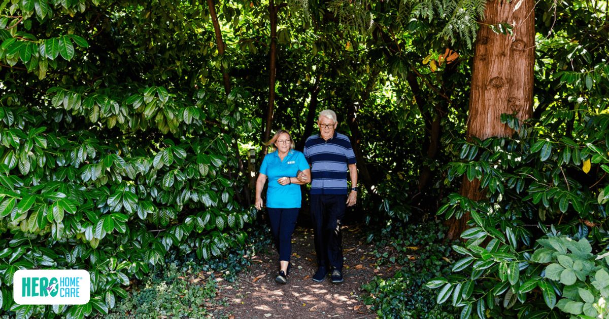 Hero Home Care caregiver walking beside senior man outdoors, supporting daily caregiving needs