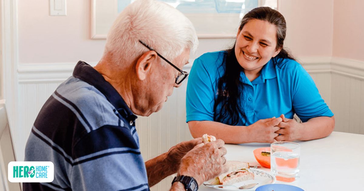 A caregiver provides mealtime support and companionship to an older man, demonstrating how home care can help a senior stay at home more safely.