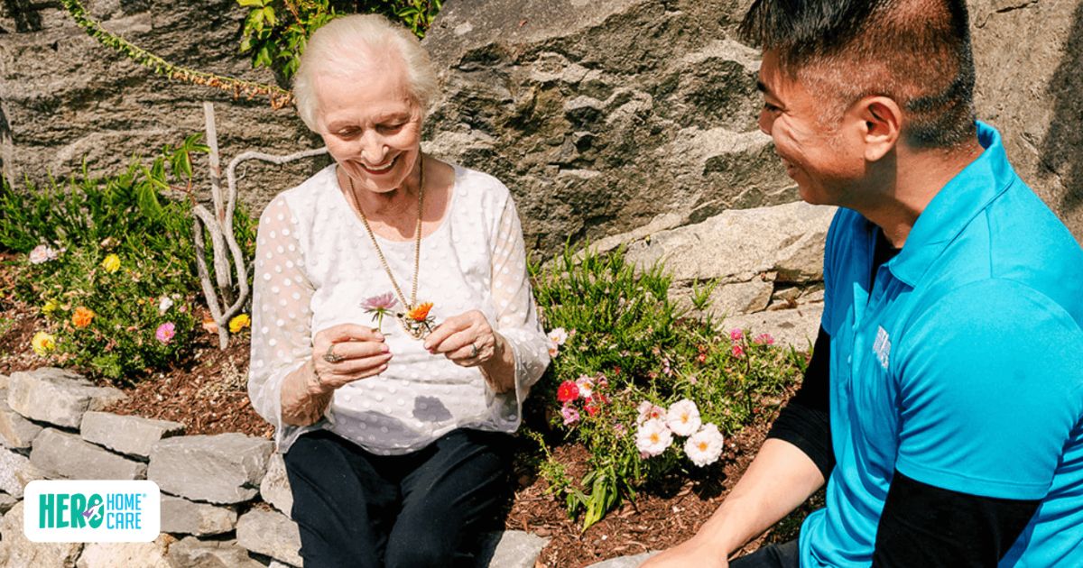 A smiling elderly woman enjoys gardening with her caregiver in a bright outdoor setting, highlighting the companionship and engaging activities provided by dementia home care support.