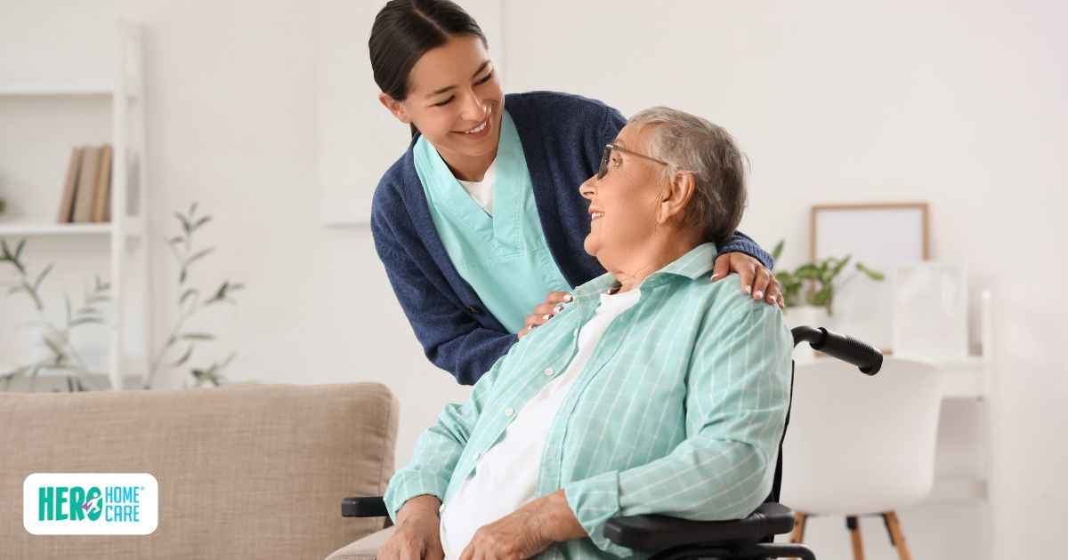 A smiling caregiver rests her hands on the shoulders of an elderly woman in a wheelchair, illustrating how professional support helps navigate recovery timelines after surgery at home.
