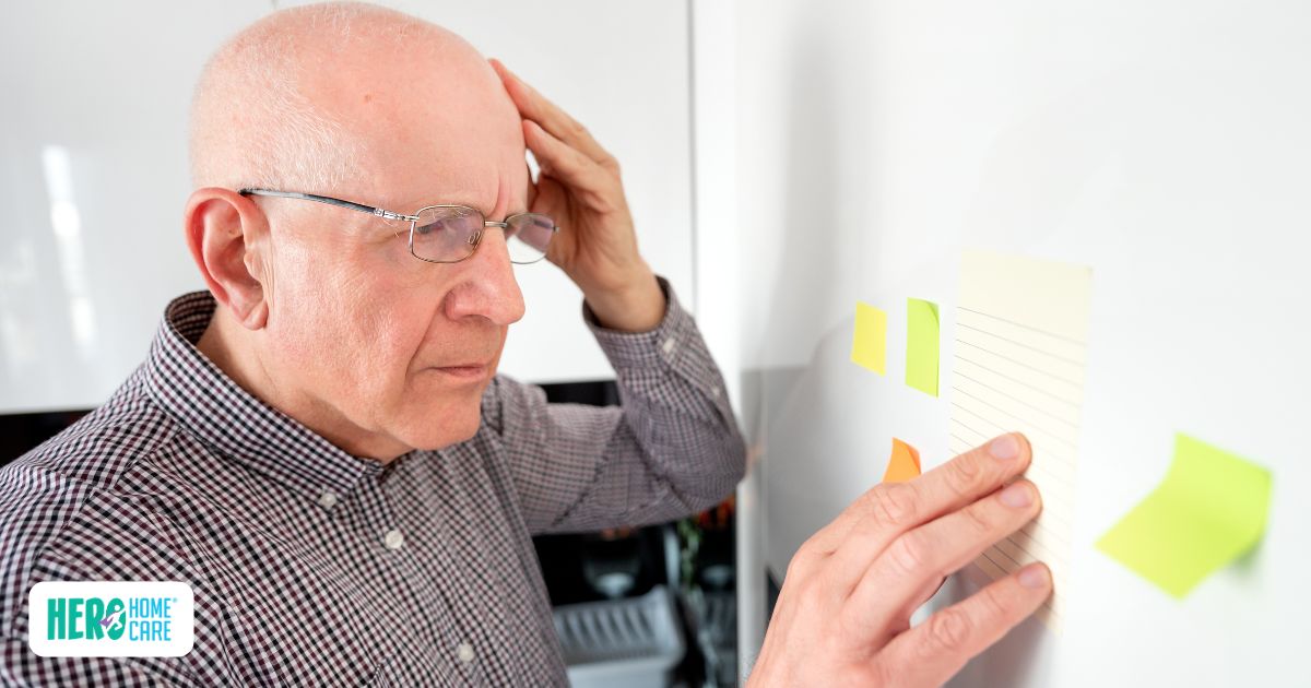 An elderly man looking confused while touching a sticky note on a wall, depicting one of the common warning signs of dementia.