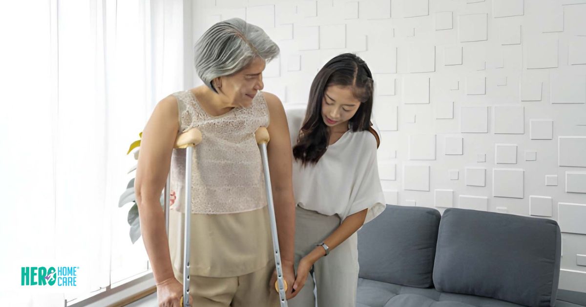 Senior woman using crutches being gently assisted by a caregiver in a bright modern living room