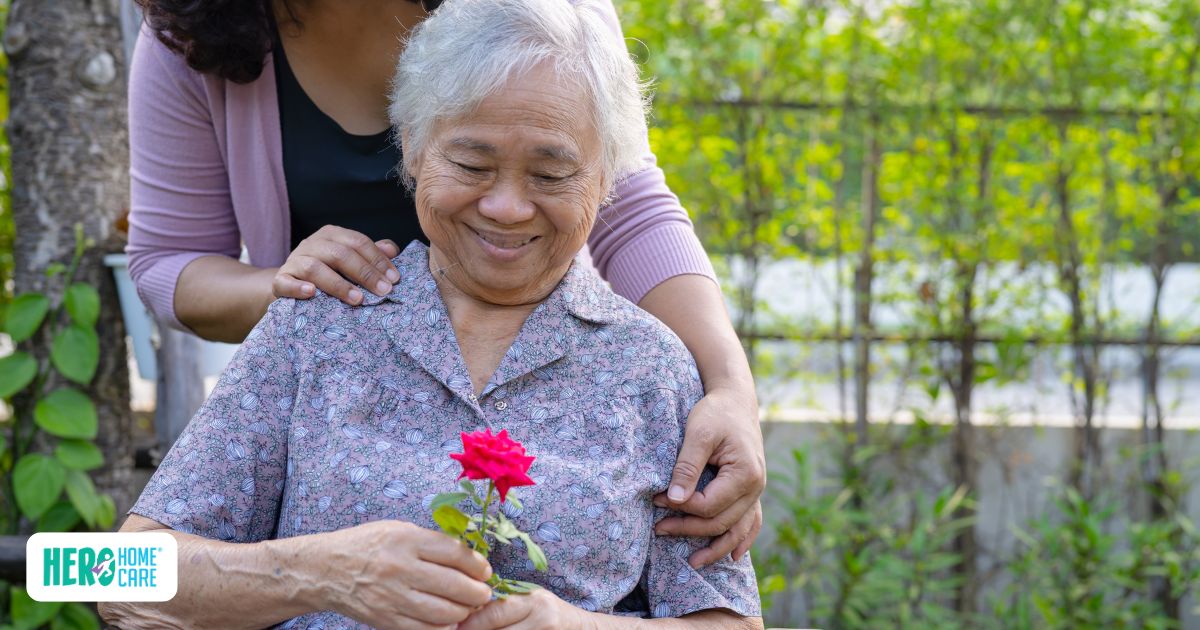 Senior holding a flower during an outdoor sensory activity with caregiver support, illustrating therapeutic engagement and connection in dementia care