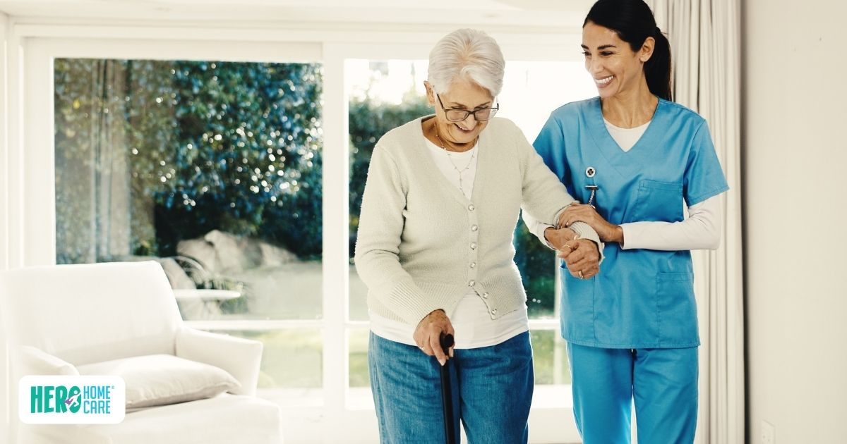 Older adult using a cane while receiving mobility support from a caregiver at home, showing assistance with safe movement and daily activities for a senior living with mobility challenges.