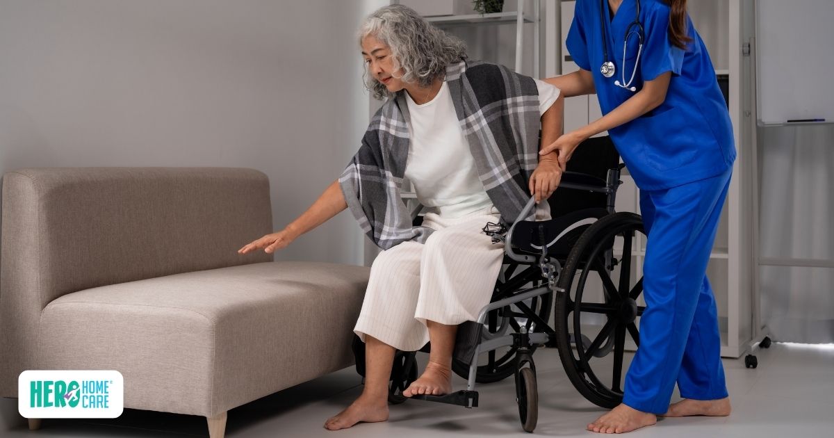 Caregiver assisting an older adult with limited mobility as she transfers from a wheelchair to a chair.